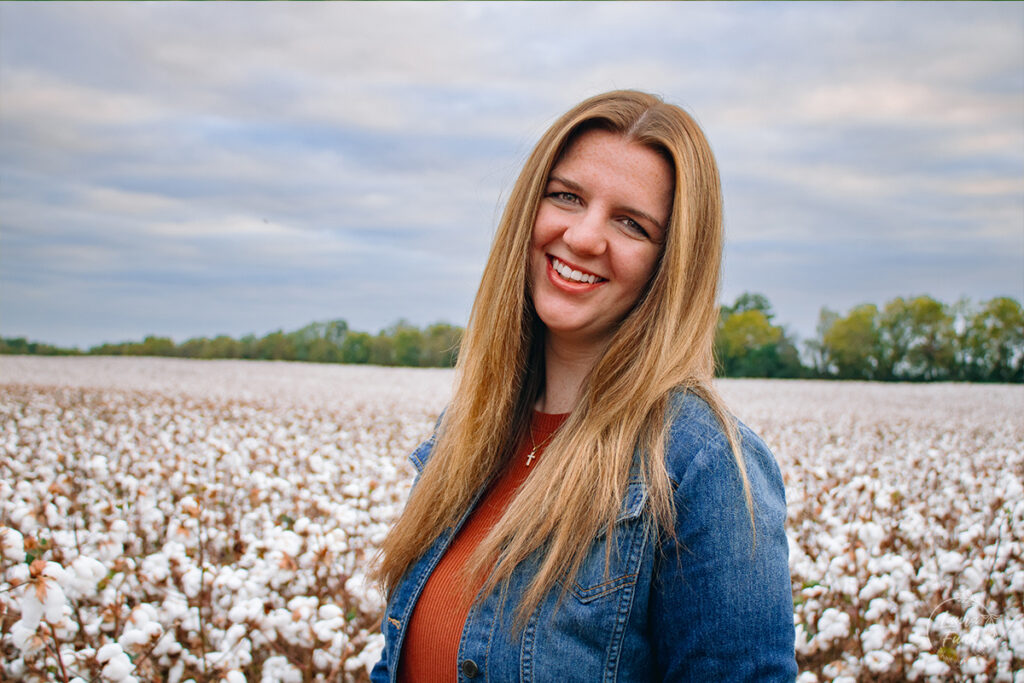 girl posing for senior photo with a cotton field behind her