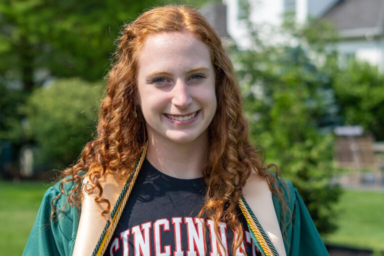 graduate student posing on campus with a big grin