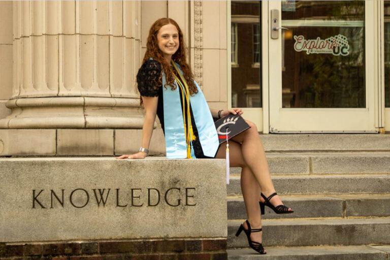 Girl posing for senior portrait on the step of her college