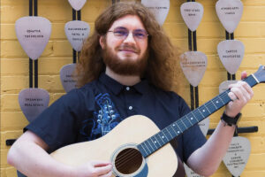 a guy holding his guitar and posing for his senior portrait