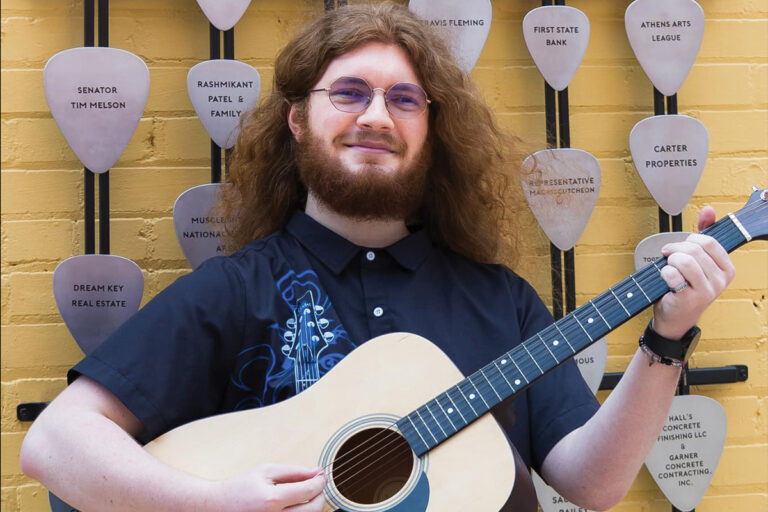 a guy holding his guitar and posing for his senior portrait