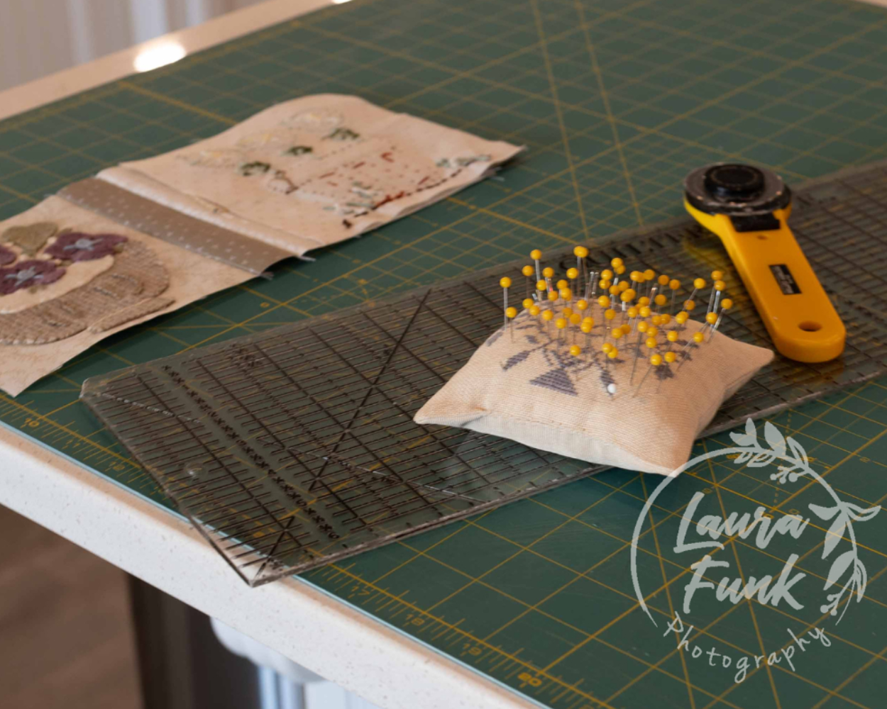 Sewing workspace with a pin cushion full of yellow-headed pins on a cutting mat and a yellow rotary cutter nearby; fabric scraps in the background.