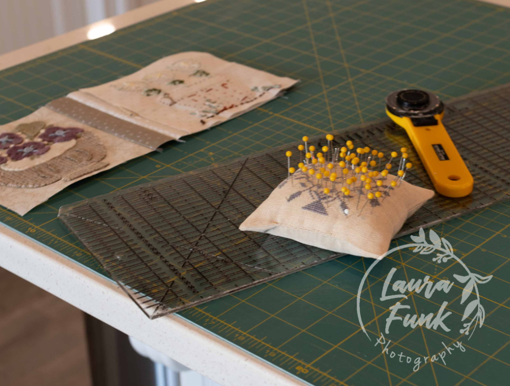Sewing workspace with a pin cushion, rotary cutter, and fabric pieces on a cutting mat.